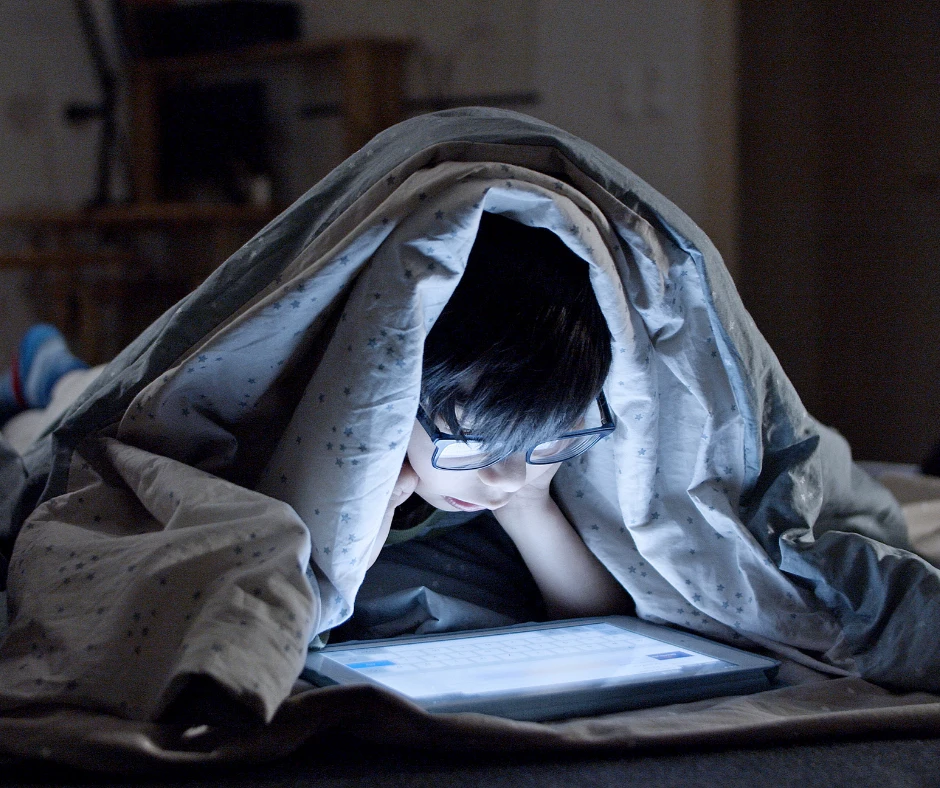 Niño viendo la tablet en la cama antes de dormir